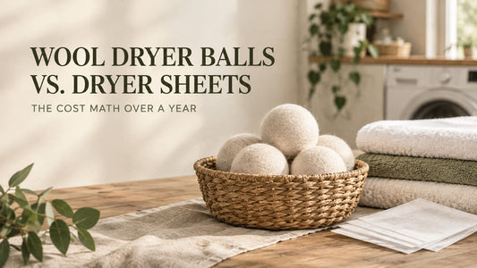 A woven basket filled with white wool dryer balls alongside a stack of folded towels and a small pile of dryer sheets, with the text "Wool Dryer Balls vs. Dryer Sheets: The Cost Math Over a Year."
