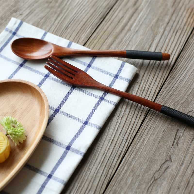 Wooden spoon and fork with dark wrapped handles resting on a blue-checked linen napkin
