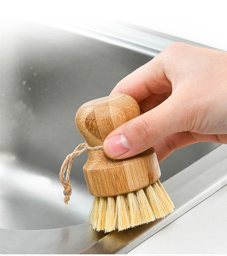 Hand holding a round bamboo dish brush with natural fiber bristles over a stainless steel sink